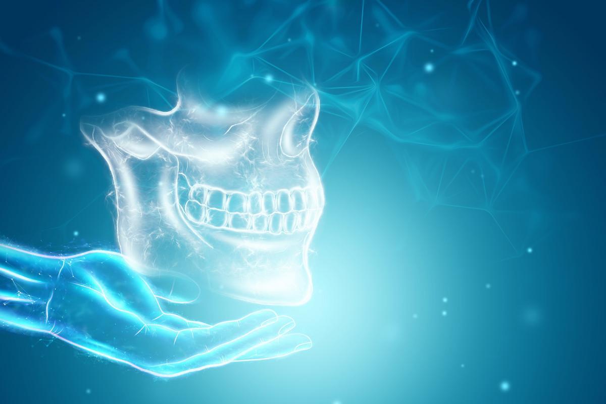 A glowing digital model of a human skull and jaw hovers above an outstretched hand.